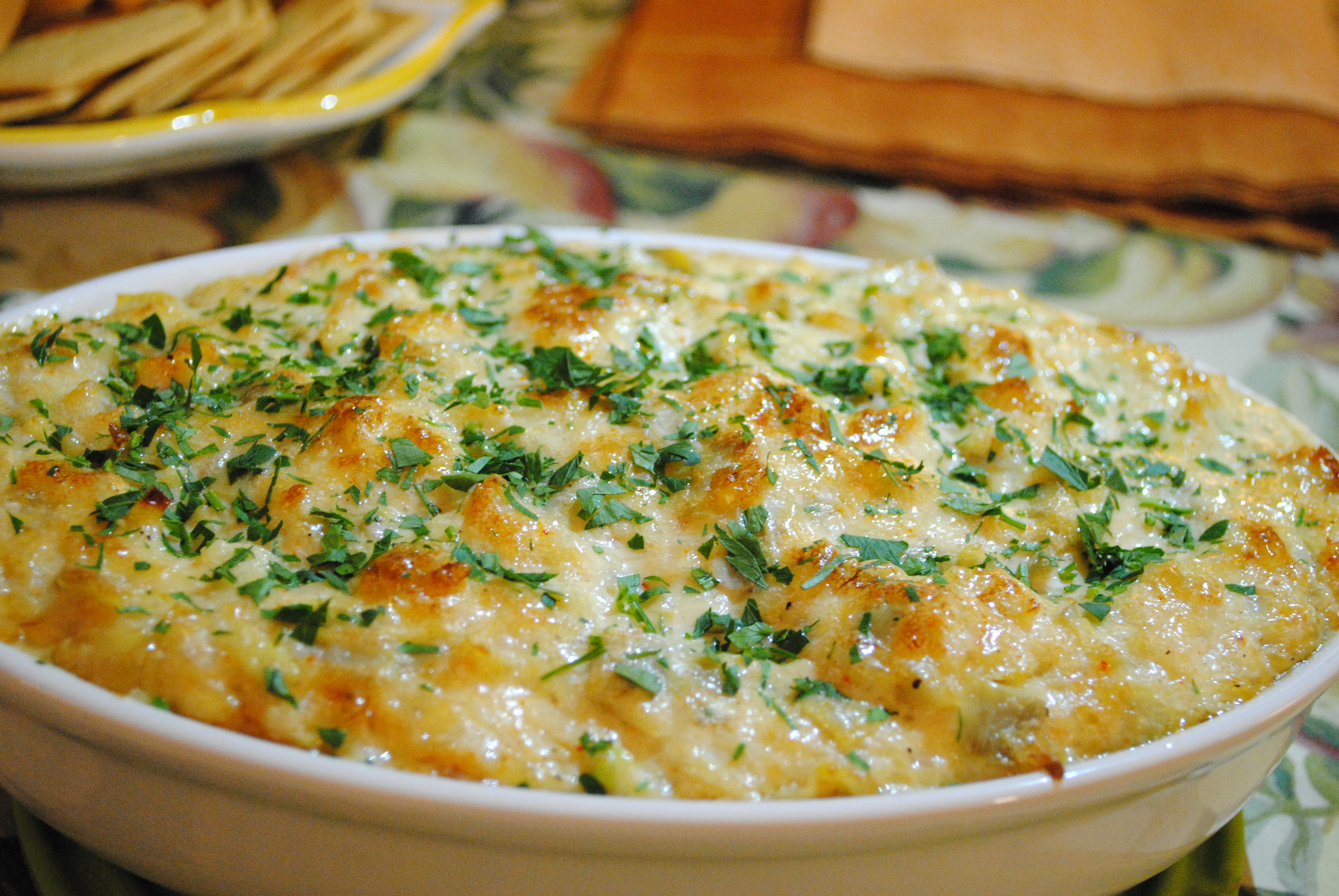 crab dip garnished with parsley, crackers and a patterned tablecloth in background