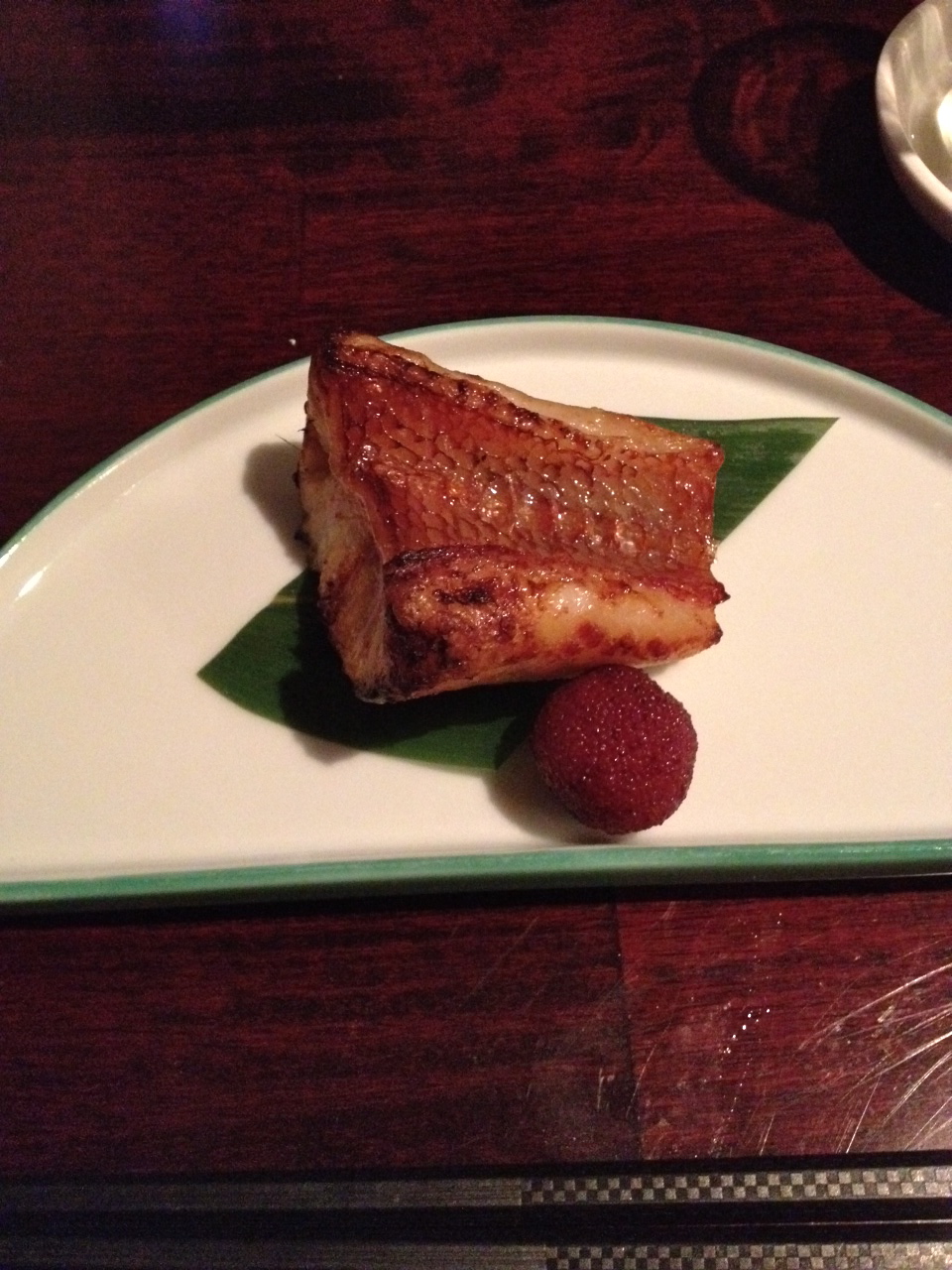 grilled thornyhead filet served on a semicircular plate with red garnish 