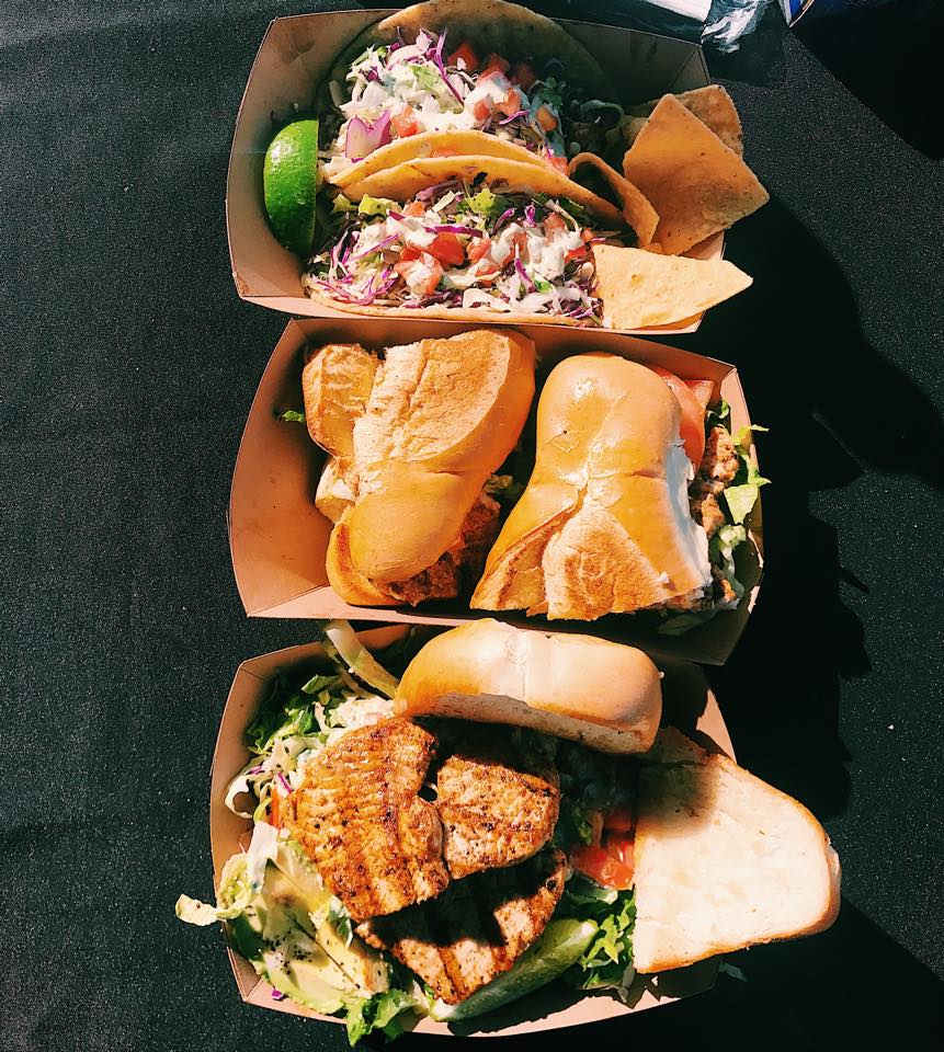 three paper trays arranged vertically with fish tacos and fish sandwiches