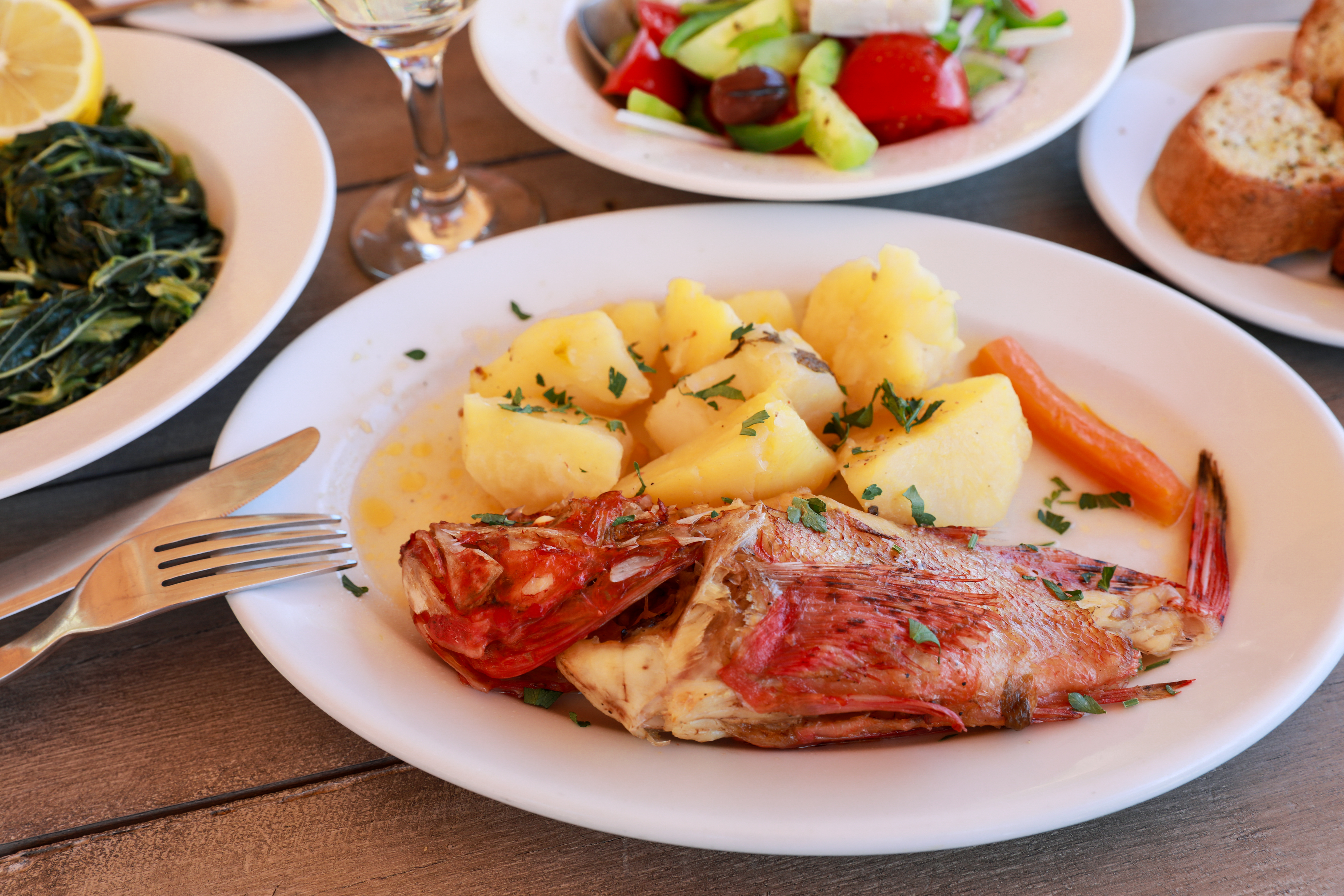 red scorpionfish with potatoes and plates of vegetables and bread 