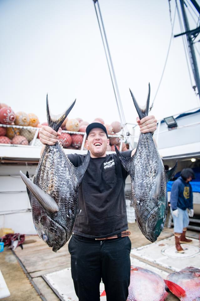 fisherman holding two sickle pomfrets, another fisherman and two opah fish in the background