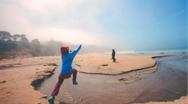 child jumping over a stream of water flowing through a beach