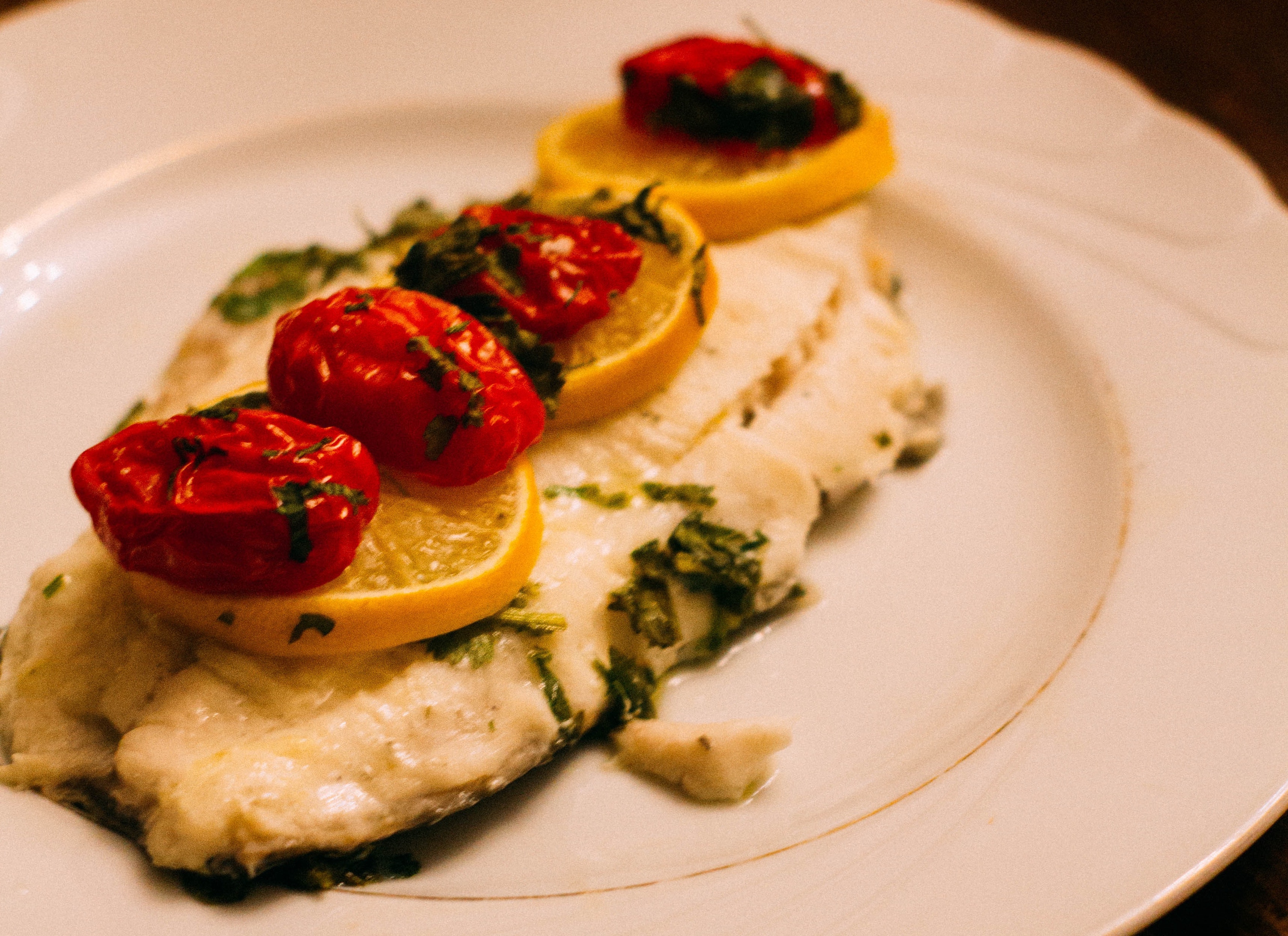 whitefish filet topped with lemon and cherry tomatoes, garnished with greens 